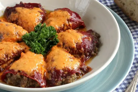 Pimientos rellenos de carne cubiertos con una cremosa salsa naranja, adornados con perejil fresco.
