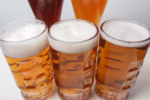 Tre bicchieri di birra dorata con schiuma bianca, uno più scuro e uno arancione sullo sfondo. Un invito a scoprire la differenza tra pils e lager.