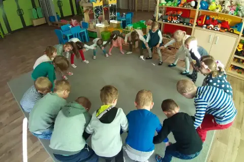 Dzieci w przedszkolu biorą udział w zabawach integracyjnych, tworząc krąg i wykonując ćwiczenia.