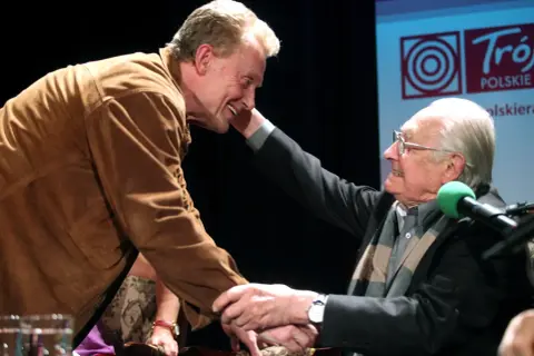 Dwóch starszych panów, jeden w brązowej kurtce, drugi w garniturze, ściska sobie dłonie. Może to symboliczne zakończenie prawdziwych powodów konfliktu reżysera z główną gwiazdą polskiej produkcji?