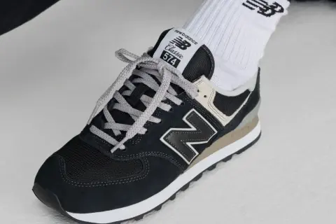 Klasyczne czarne buty sportowe new balance wl 574 z szarymi sznurówkami i beżowymi akcentami, noszone z białymi skarpetkami z logo.