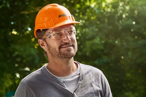 Hombre con casco naranja y gafas de seguridad, listo para usar su epi desbrozadora.