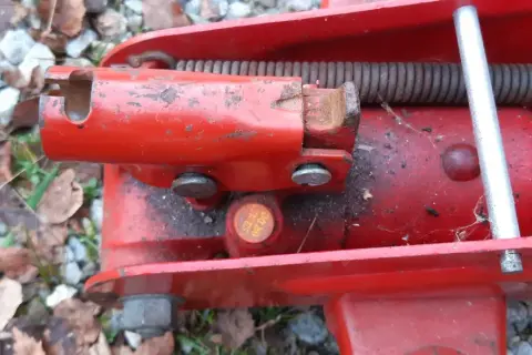 Detaljbild av en röd domkraft. En metallpinne sticker upp och en fjäder är synlig. Det ser ut som att det är dags att fylla olja i domkraften för att den ska fungera som den ska.