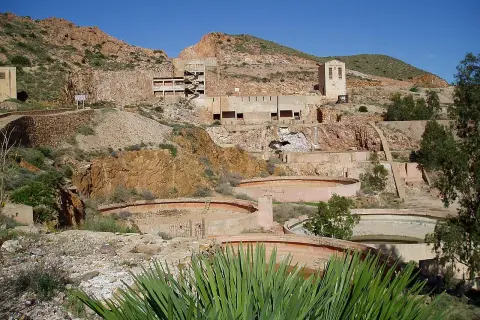 Ruinas de las minas Rodalquilar, con edificios abandonados y balsas circulares en un paisaje árido bajo un cielo azul.