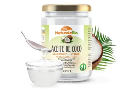 Un frasco de aceite de coco NaturaleBio, con una cuchara vertiendo el aceite en un cuenco. El aceite de coco es bueno para el pelo.