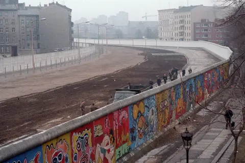 Kolorowy mur berliński, który wybudował NRD, z widocznymi ludźmi i budynkami w tle.