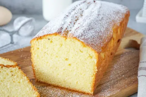Ein saftiger Rührkuchen, bestäubt mit Puderzucker, ideal für einfache Kuchen Rezepte. Daneben liegen zwei Scheiben.