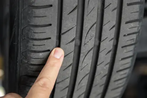 Un doigt pointe un pneu craquelé, montrant l'usure et les fissures qui compromettent la sécurité.