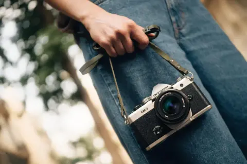 Dłoń trzyma aparat OM-3, przypominając o czasach, kiedy powstał aparat fotograficzny.