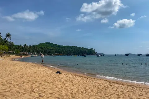 Piękna plaża z palmami, łodzie na turkusowym morzu i zielona wyspa. To idealne miejsce na odkrywanie Wietnamu na własną rękę.