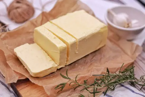 Smörblock skuret i bitar på bakplåtspapper, med rosmarin och vitlök i bakgrunden. Tänk dig att detta smör förvandlas till klarifierat smör, eller ghee, för en rikare smak.