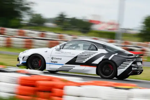 Biało-czarne Alpine A110 z logotypami Castrol i Delphi pędzi po torze wyścigowym, zostawiając za sobą rozmyte bariery.