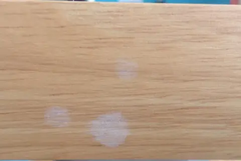 Trois petites taches blanches sur une surface en bois clair, comme des traces laissées par des gouttes d'eau séchées.