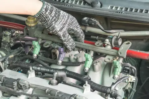 Main d'un mécanicien ganté manipulant le rail d'injection pour tester injecteur diesel.