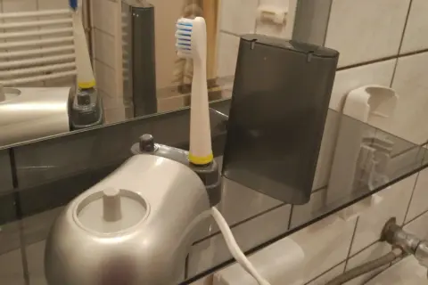Elektroniczna szczoteczka do zębów i jej wymienna końcówka stoją na szklanej półce, pokazując, jak przechowywać szczoteczki do zębów w łazience.