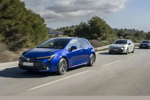Niebieska Toyota Corolla hatchback, model hybrydowy, jedzie po krętej drodze wśród zielonych wzgórz.