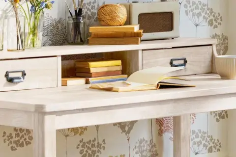 Scrivania chiara con cassetti, libri, tazza e radio vintage. Ideale per chi vuole imparare come verniciare un mobile da marrone a bianco.