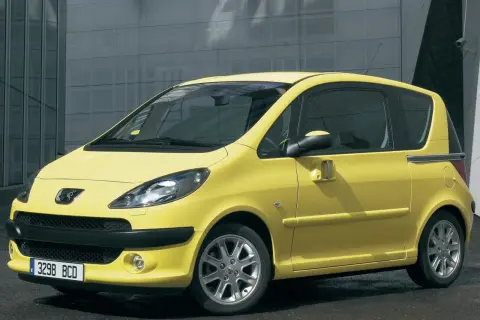 Żółty Peugeot 1007 z przesuwnymi drzwiami na tle nowoczesnego budynku.
