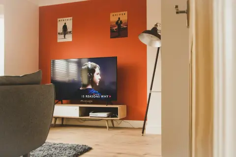 Salon z kanapą i telewizorem wyświetlającym serial. Ściana w intensywnym, **kolorze pomarańczowym** dodaje energii wnętrzu.
