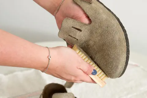 Hände reinigen Wildlederschuh mit Bürste. So lassen sich hartnäckige blutflecken aus leder entfernen und das Material wird wieder wie neu.