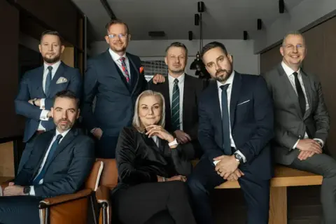 Grupa siedmiu profesjonalistów w garniturach, w tym jedna kobieta, pozuje do zdjęcia.