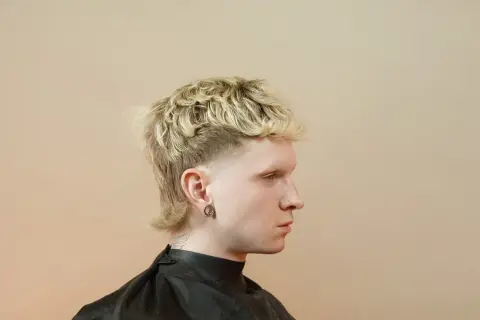 Młody mężczyzna z blond, kręconymi włosami i charakterystyczną fryzurą mullet.