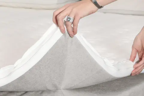 Hände ziehen den Reißverschluss eines Toppers ab, um die **Boxspringbett Pflege** zu erleichtern.