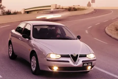 En silverfärgad Alfa Romeo 156 kör på en kurvig väg i solnedgången.