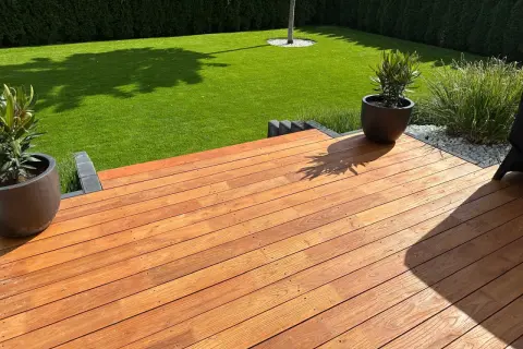 Terraza de madera de robinia con césped verde y plantas en macetas.