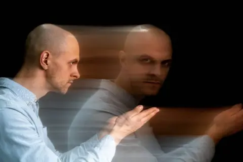 Uomo calvo con effetto mosso, sembra diviso tra due stati, un'immagine che evoca un disturbo del controllo.