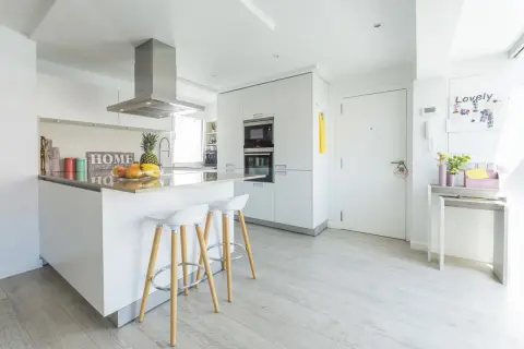 Cocinas modernas blancas con isla central, taburetes y electrodomésticos integrados. Un espacio luminoso y funcional.
