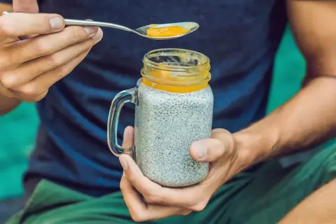 Mann hält ein Glas Chia-Pudding mit Mango-Topping. Die Frage "wieviel chiasamen pro tag" wird durch die gesunde Mahlzeit beantwortet.