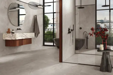 Salle de bain moderne avec baignoire îlot, douche vitrée et lavabo suspendu. La faïence grise habille les murs et le sol, créant une ambiance épurée et luxueuse.