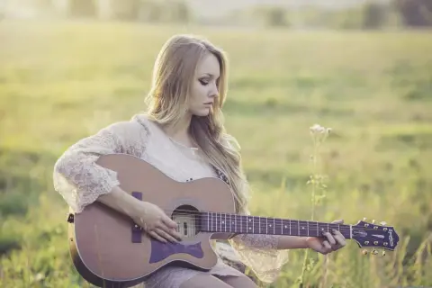 Dziewczyna gra na gitarze w plenerze. Czy wiesz, że gitara akustyczna ma swoje ciekawostki o muzyce?