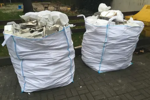 Dwa białe worki na gruz z niebieskimi szwami, gotowe do odbioru. W środku widać resztki materiałów budowlanych.