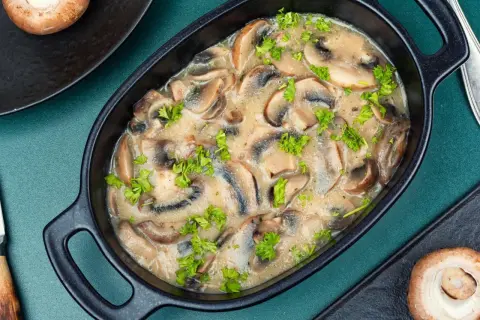 Aksamitny sos pieczarkowy z mascarpone, udekorowany natką pietruszki, w czarnej miseczce.