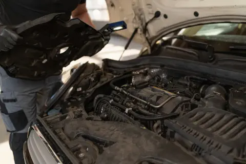 Mechanik sprawdza silnik, szukając objawów przegrzania. Widać elementy silnika i narzędzia.