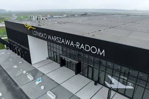 Nowoczesny budynek lotniska Warszawa-Radom z napisem "ODLOTY" i symbolem samolotu na szkle.