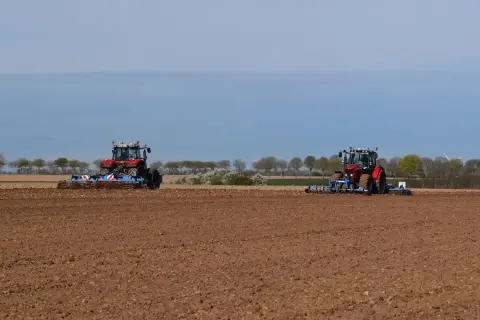 Deux tracteurs préparent le sol pour la culture du lin. Le champ est labouré, prêt pour les semis.