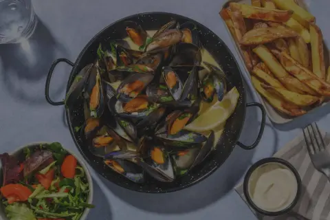 Un plat de moules frites, accompagné d'une salade fraîche et d'une sauce crémeuse. Un délice pour les amateurs de fruits de mer.