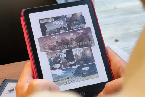 Une personne lit une bande dessinée d'action sur un cbz kindle. Des onomatopées comme "BLAM" et "RATATATA" parsèment les cases.