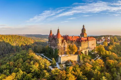 Zamek Książ w malowniczej kotlinie kłodzkiej, otoczony jesiennymi barwami lasów, prezentuje się majestatycznie na tle błękitnego nieba.