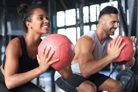 Coppia sorridente si allena in palestra con palle mediche. Non preoccuparti se il primo mese di palestra si ingrassa, è normale!