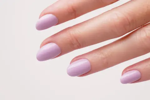 Une main aux ongles courts et arrondis, peints d'un joli violet pastel. Une idée ongle violet douce et élégante.
