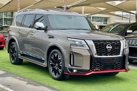 Szary Nissan Patrol 2025 Nismo z czerwonymi akcentami, prezentujący się na zielonej trawie.