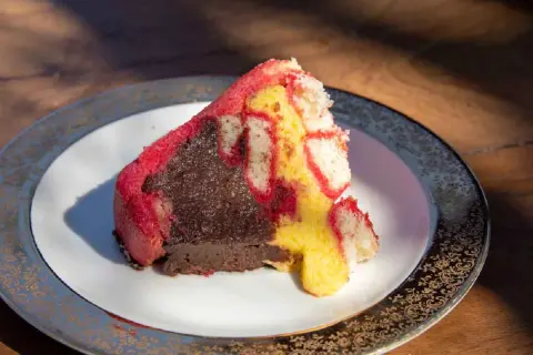 Una fetta di zuppa inglese, con pan di Spagna rosso e giallo e crema al cioccolato, su un piatto decorato.