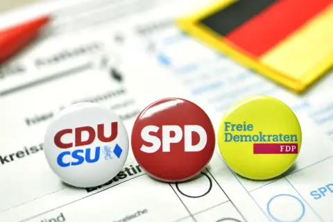 Anstecker von CDU/CSU, SPD und FDP liegen auf einem Wahlzettel. Die deutsche Flagge im Hintergrund symbolisiert die politische Landschaft für eine mögliche Deutschland Koalition.