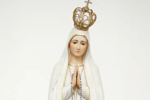 Figurka Matki Bożej Fatimskiej w białym welonie i złotej koronie, z rękami złożonymi do modlitwy.