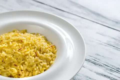 Un crémeux risotto à la milanaise, parsemé de fils de safran, dans une assiette blanche sur fond de bois.