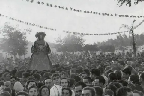 Una figura alta, vestida con traje tradicional, se alza sobre una multitud. Es parte de la **historia del Rocío**, una tradición ancestral.
